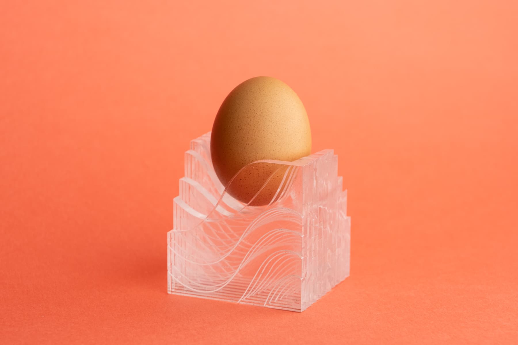 EggHolder 9, an incomplete cube made of stacked acrylic pieces, holding an egg against a salmon-colored background.
