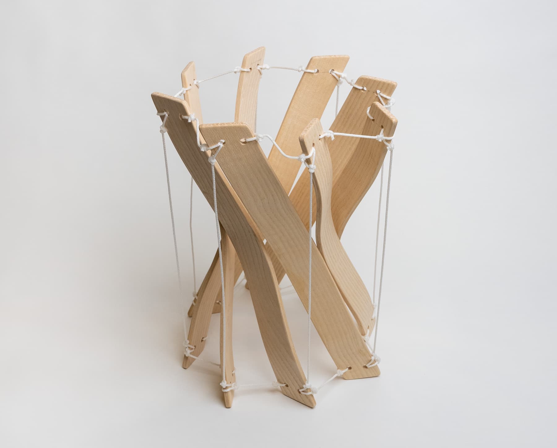 A twisted prism made out of 8 identical bent lamination pieces held together by a series of white strings.